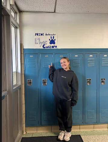 Elyse standing beside her PRIDE Ambassador poster by her locker.